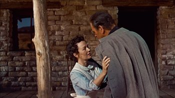 Movie still from “The Searchers” (1956), directed by John Ford – A woman standing next to a man in front of a brick wall; Medium shot, Low angle
