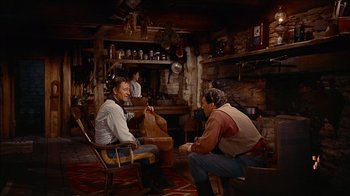 Movie still from “The Searchers” (1956), directed by John Ford – Two men sitting in chairs in front of a fireplace; Wide shot, Over the shoulder angle