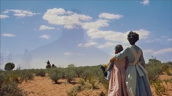 Movie still from “The Searchers” (1956), directed by John Ford – Two people in a field looking at a mountain in the distance; Wide shot, Low angle