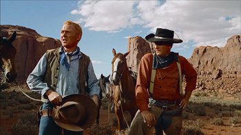 Movie still from “The Searchers” (1956), directed by John Ford – Two men in cowboy hats standing next to horses; Medium shot, Low angle