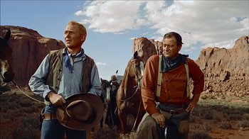 Movie still from “The Searchers” (1956), directed by John Ford – Two men are standing in front of a herd of horses; Medium shot, Low angle