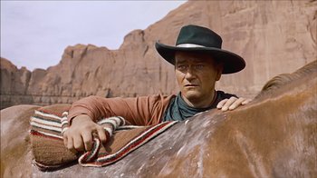 Movie still from “The Searchers” (1956), directed by John Ford – A man wearing a cowboy hat and holding on to a horse; Medium shot, Low angle
