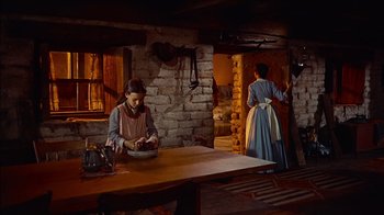 Movie still from “The Searchers” (1956), directed by John Ford – Two women dressed in period clothing work in a kitchen; Wide shot, High angle