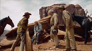 Movie still from “The Searchers” (1956), directed by John Ford – A group of men standing on top of a dirt hill; Wide shot, Low angle
