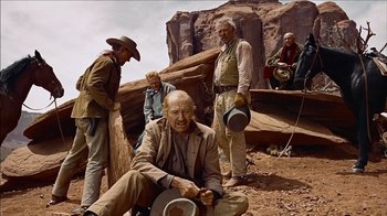 Movie still from “The Searchers” (1956), directed by John Ford – A group of men standing on top of a dirt field; Wide shot, Low angle