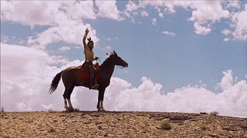Movie still from “The Searchers” (1956), directed by John Ford – A man riding on the back of a brown horse on top of a hill; Wide shot, Low angle