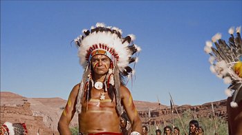 Movie still from “The Searchers” (1956), directed by John Ford – A man in a native american headdress standing in front of a group of people; Medium shot, Low angle