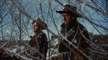 Movie still from “The Searchers” (1956), directed by John Ford – Two men standing next to each other on a snowy day; Medium shot, Low angle