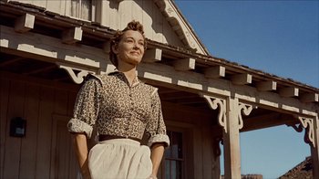 Movie still from “The Searchers” (1956), directed by John Ford – A woman standing in front of a wooden house; Medium shot, Low angle