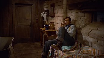 Movie still from “The Searchers” (1956), directed by John Ford – A man sitting on a chair in a living room; Wide shot, High angle