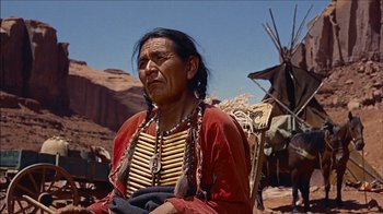Movie still from “The Searchers” (1956), directed by John Ford – An older woman wearing a red jacket and a yellow shirt; Medium shot, Low angle