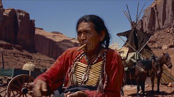 Movie still from “The Searchers” (1956), directed by John Ford – An older native american man smoking a pipe; Medium shot, Low angle