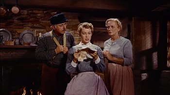 Movie still from “The Searchers” (1956), directed by John Ford – An older couple and a young girl looking at a piece of paper in front of a fireplace; Medium shot, Low angle