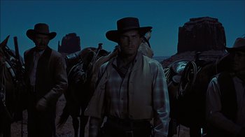 Movie still from “The Searchers” (1956), directed by John Ford – A man in a cowboy hat standing next to a horse; Medium shot, Low angle