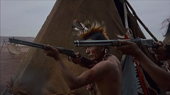 Movie still from “The Searchers” (1956), directed by John Ford – A man with a gun in his hand is holding a rifle in his other hand; Medium shot, Low angle