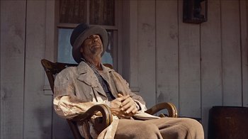 Movie still from “The Searchers” (1956), directed by John Ford – A man sitting in a chair wearing a hat; Medium shot, Low angle