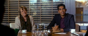 Movie still from “The Second Best Exotic Marigold Hotel” (2015), directed by John Madden – Two people sitting at a wooden table in front of a window; Medium shot, Over the shoulder angle