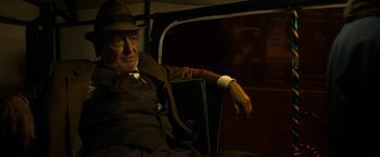 Movie still from “The Second Best Exotic Marigold Hotel” (2015), directed by John Madden – An older man sitting on a bus with his arm resting on the arm rest; Medium shot, Over the shoulder angle