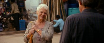 Movie still from “The Second Best Exotic Marigold Hotel” (2015), directed by John Madden – An older woman smiles while holding a yellow cloth; Close Up shot, Over the shoulder angle