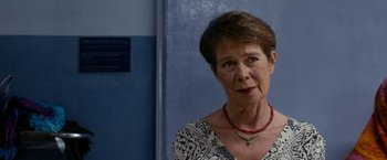 Movie still from “The Second Best Exotic Marigold Hotel” (2015), directed by John Madden – An older woman wearing a necklace and looking at the camera; Close Up shot, Over the shoulder angle