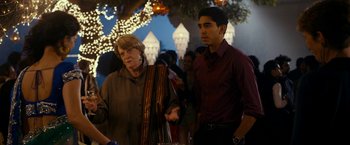 Movie still from “The Second Best Exotic Marigold Hotel” (2015), directed by John Madden – A man and a woman standing next to each other in front of lights; Medium shot, Over the shoulder angle