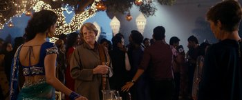 Movie still from “The Second Best Exotic Marigold Hotel” (2015), directed by John Madden – An older woman standing in front of a group of people; Medium shot, Over the shoulder angle