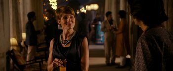 Movie still from “The Second Best Exotic Marigold Hotel” (2015), directed by John Madden – A woman in a black dress is holding a glass of orange juice; Medium shot, Over the shoulder angle