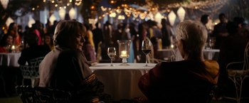 Movie still from “The Second Best Exotic Marigold Hotel” (2015), directed by John Madden – A woman sitting at a table in front of a glass of wine; Medium shot, Over the shoulder angle