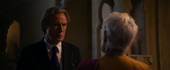 Movie still from “The Second Best Exotic Marigold Hotel” (2015), directed by John Madden – An older man in a suit and tie talking to an older woman in a suit; Close Up shot, Over the shoulder angle
