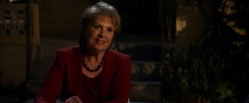 Movie still from “The Second Best Exotic Marigold Hotel” (2015), directed by John Madden – A person wearing a suit and a necklace; Close Up shot, Over the shoulder angle