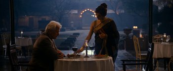 Movie still from “The Second Best Exotic Marigold Hotel” (2015), directed by John Madden – A man and a woman at a table with a glass of red wine; Medium shot, Over the shoulder angle