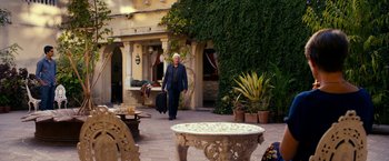 Movie still from “The Second Best Exotic Marigold Hotel” (2015), directed by John Madden – An older man carrying a suit case walks through a courtyard; Wide shot, Over the shoulder angle