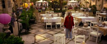 Movie still from “The Second Best Exotic Marigold Hotel” (2015), directed by John Madden – An older woman standing in front of an outdoor dining area; Wide shot, High angle