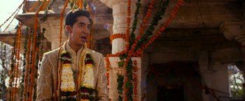 Movie still from “The Second Best Exotic Marigold Hotel” (2015), directed by John Madden – A man in a white shirt and flowers around his neck; Medium shot, Over the shoulder angle