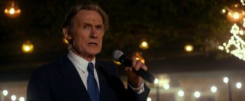 Movie still from “The Second Best Exotic Marigold Hotel” (2015), directed by John Madden – A man in a suit and tie holding a microphone; Close Up shot, Low angle