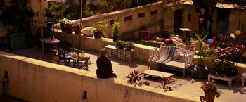 Movie still from “The Second Best Exotic Marigold Hotel” (2015), directed by John Madden – A woman sitting on a ledge in a courtyard; Extreme Wide shot, High angle