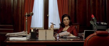 Movie still from “The Secret in Their Eyes” (2009), directed by Juan José Campanella – A woman sitting at a desk holding a pen and paper; Medium shot, Over the shoulder angle