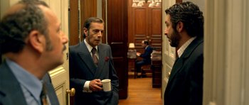 Movie still from “The Secret in Their Eyes” (2009), directed by Juan José Campanella – A man in a suit and tie holding a coffee mug; Medium shot, Over the shoulder angle