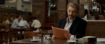 Movie still from “The Secret in Their Eyes” (2009), directed by Juan José Campanella – A man sitting at a table reading a piece of paper; Medium shot, Over the shoulder angle