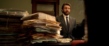 Movie still from “The Secret in Their Eyes” (2009), directed by Juan José Campanella – A man standing in front of a pile of papers; Medium shot, Low angle