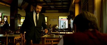 Movie still from “The Secret in Their Eyes” (2009), directed by Juan José Campanella – A man wearing a suit and tie standing at a table in a restaurant; Medium shot, Low angle