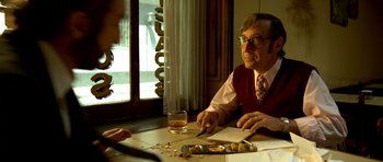 Movie still from “The Secret in Their Eyes” (2009), directed by Juan José Campanella – An older man sitting at a table with a glass of wine; Medium shot, Over the shoulder angle