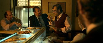 Movie still from “The Secret in Their Eyes” (2009), directed by Juan José Campanella – Two men are sitting at a table in front of a display case; Medium shot, Over the shoulder angle