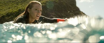 Movie still from “The Shallows” (2016), directed by Jaume Collet-Serra – A woman in a wetsuit riding a surfboard in the ocean; Close Up shot, Low angle