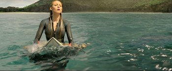 Movie still from “The Shallows” (2016), directed by Jaume Collet-Serra – A woman in a wetsuit holding a surfboard in a body of water; Medium shot, High angle