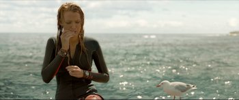 Movie still from “The Shallows” (2016), directed by Jaume Collet-Serra – A woman in a wet suit sitting on the beach; Medium shot, Over the shoulder angle