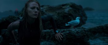 Movie still from “The Shallows” (2016), directed by Jaume Collet-Serra – A woman in a wetsuit leaning on a rock near a body of water; Medium shot, Low angle