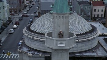 Movie still from “The Siege” (1998), directed by Edward Zwick – A man taking a picture of a building from a tower; Extreme Wide shot, Overhead angle