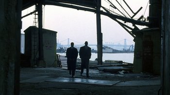 Movie still from “The Siege” (1998), directed by Edward Zwick – Two men in suits are standing next to the water; Extreme Wide shot, Low angle