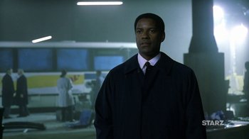 Movie still from “The Siege” (1998), directed by Edward Zwick – A man standing in a dark room with lights in the background; Medium shot, Low angle